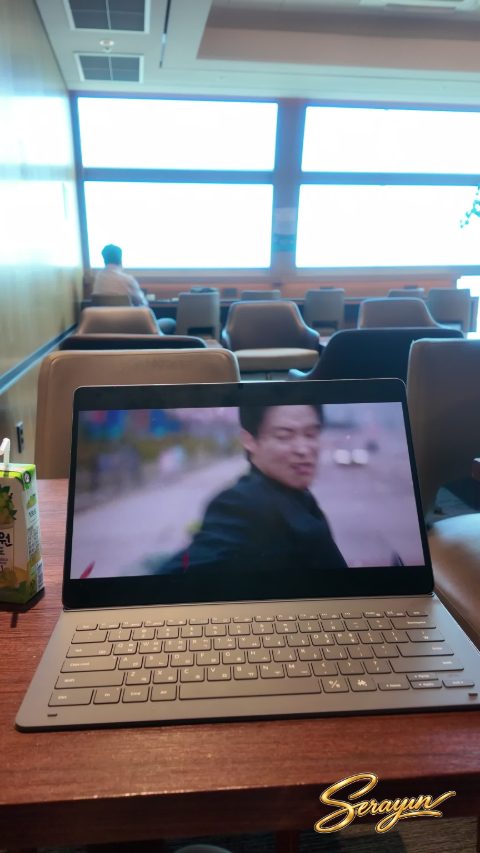 공항 라운지 좌석과 큰 창을 배경으로 테이블 위에 태블릿과 음료가 놓인 장면